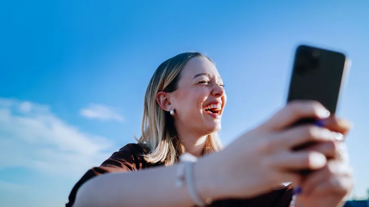 Eine junge Frau lacht und schaut auf ihr Smartphone